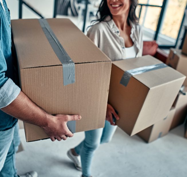 A young married couple in the living room in the house unpack boxes with things. Happy husband and wife are having fun, are looking forward to a new home. Moving, buying a house, apartment concept.